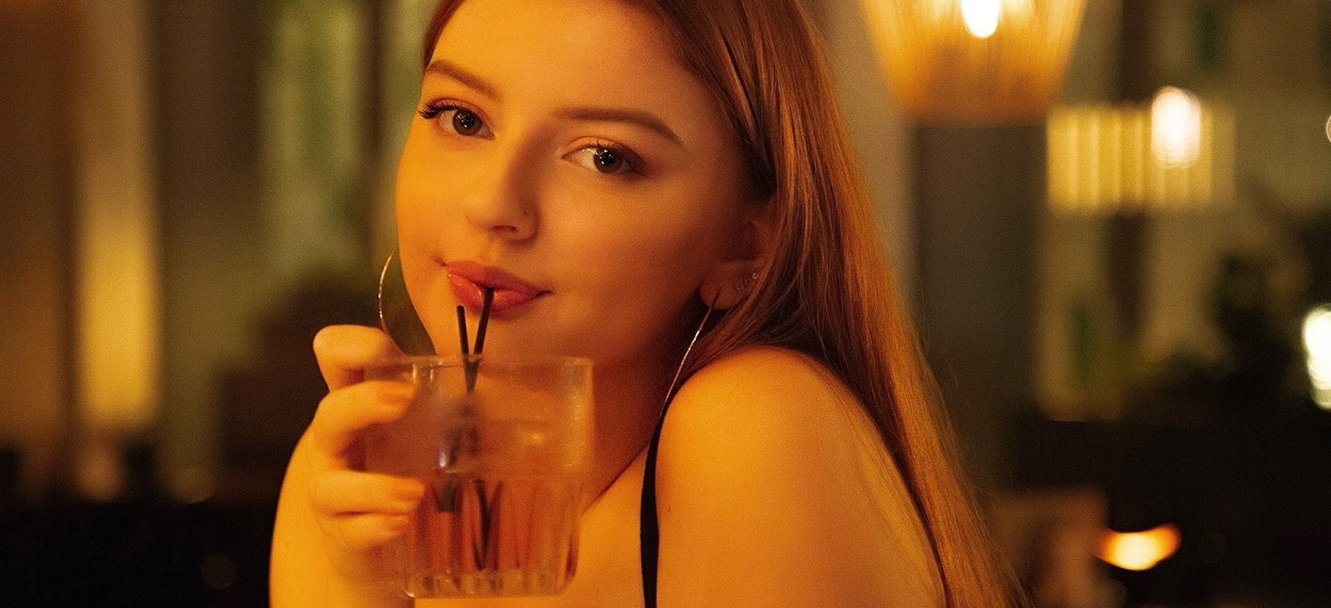 Woman smiling and sipping a drink at a warmly lit bar, representing the real-world spark Chat Me Up is built around